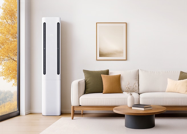 가을 풍경이 보이는 거실에 흰색 LG 휘센 쿨 에어컨과 베이지색 소파, 원형 테이블이 놓인 따뜻한 인테리어 공간.